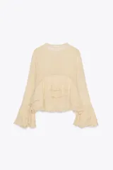 Camisa de viscosa con cuello redondo y escote en pico ajustable mediante lazadas. Presenta cierre frontal con botones, mangas largas con terminación evasé y detalle de volantes en el mismo tejido.