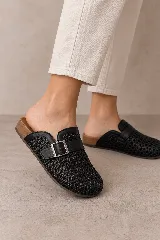 Zueco cerrado de punta redondeada color marfil con diseño trenzado, tira superior con hebilla metálica y suela plana.