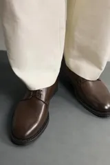 Zapato de vestir tipo derby marrón oscuro, con parte superior lisa y suela con ligero tacón.