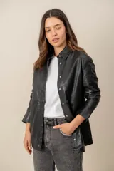 Campera estilo sobrecamisa confeccionada en cuero negro, de corte recto, con cuello camisero y cierre frontal de botones metálicos a presión.