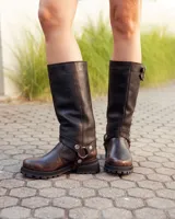 Bota de caña alta confeccionada en cuero color marrón caoba con acabado desgastado. Presenta una suela track robusta, correas con hebillas en la parte superior de la caña y un arnés decorativo con herrajes metálicos en el tobillo.