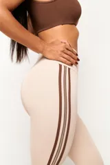 Calza deportiva de tiro alto en color azul grisáceo, con diseño de tres líneas verticales en color crema en los laterales. Confeccionada en tejido técnico de alta compresión, presenta un corte sin costura frontal para mayor comodidad.