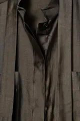 Camisa de corte holgado confeccionada en mezcla de lyocell con acabado satinado. Presenta cuello redondo con lazadas integradas, cierre frontal con botones ocultos bajo solapa, bolsillos de plastrón en el frente y mangas largas con puños anchos. El bajo es asimétrico y redondeado.