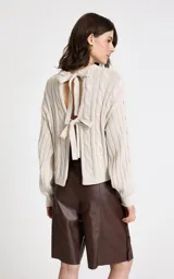 Sweater de punto beige con diseño de trenzas verticales, cuello redondo acanalado, mangas largas con puños ajustados y dobladillo acanalado.