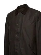 Chaqueta encerada de estilo clásico, color marrón oscuro, con cuello de cotelé y cierre frontal mediante broches a presión. Presenta un diseño de corte regular con bolsillos laterales integrados.