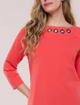 Remera blanca de algodón con elastano, de corte semi holgado, escote bote con ojalillos metálicos frontales, mangas tres cuartos raglán y ruedo asimétrico curvado.