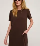 Vestido corto marrón oscuro, estilo camiseta, con escote redondo, mangas cortas y bolsillos laterales. El bajo es redondeado.
