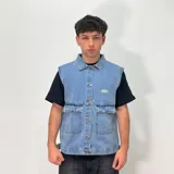 Chaleco de jean estilo oversize, con cuello camisero, cierre frontal con botones metálicos y dos bolsillos frontales con solapa. Presenta un diseño con costuras visibles y logo bordado en el pecho.
