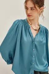 Camisa de viscosa color turquesa, de corte fluido, con cuello mao, escote en V y mangas largas abullonadas con puños elásticos.