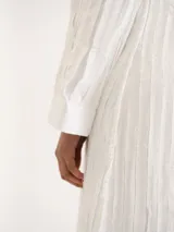 Vestido largo blanco de manga larga, cuello redondo y corte recto, con detalle de textura vertical y aberturas laterales en el bajo.