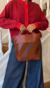Bolso tipo matera de cuero, con diseño de franjas diagonales en diferentes tonos de marrón y costuras artesanales en los bordes superiores.