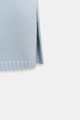 Chaleco de punto liso color celeste, con cuello redondo, manga sisa con hombros marcados y sisa ancha. El bajo tiene aberturas laterales.