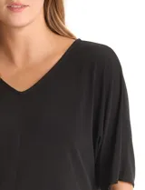 Blusa de silueta fluida con escote en V, manga japonesa corta y costura central vertical en el frente. Confeccionada en tejido de punto con acabado mate, presenta un diseño con largo asimétrico, siendo más larga en la espalda.