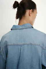 Camisa de denim de corte oversize con cuello solapa, manga larga con puños, cierre frontal con botones a presión y bolsillos de plastrón en el delantero.