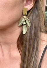 Aros colgantes con base rectangular de metal dorado texturizado, de la cual penden tres hojas metálicas en tono verde oliva y pequeñas cuentas decorativas en tonos dorados y verdes.