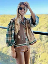 Chaleco tejido de punto con diseño asimétrico, presentando un lado en color marrón oscuro y otro en beige, ambos decorados con motivos geométricos y figuras de llamas bordadas. Posee cierre frontal con cordones de cuero y terminaciones en tejido elástico con franjas decorativas.