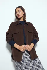 Sobrecamisa de pana color marrón oscuro, con diseño de corte amplio, cuello camisero, cierre frontal con botones y bolsillos con solapa en el pecho.