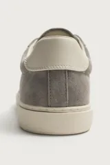Zapatilla deportiva para hombre fabricada en piel con acabado en serraje, color gris. Presenta diseño liso con detalle de contraste en el talón en tono claro y suela de goma con volumen.