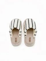 Pantuflas abiertas de estilo mule, con capellada de peluche color crema con rayas negras horizontales y plantilla de pana acanalada en tono beige.