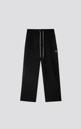 Pantalón negro de tejido técnico impermeable, corte recto y holgado, con elástico en cintura y puños. Presenta cordones ajustables con estampado repetitivo en la bragueta y un pequeño parche cuadrado con un logo de tijeras en el muslo derecho.