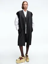 Chaleco largo reversible de diseño versátil. Por un lado, presenta una textura de peluche sintético en color marrón, y por el otro, un acabado liso. Cuenta con cierre frontal de botones y corte recto.