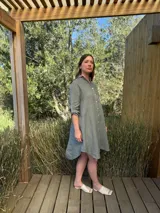 Vestido camisero color verde militar, de lino, con cuello camisero, cierre frontal con botones de nácar, manga larga con botón para recoger y bolsillo delantero. Diseño asimétrico más largo en la parte trasera.