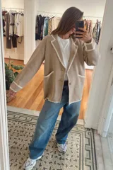 Blazer tejido de punto color beige con detalles de bordes ondulados en color blanco en solapas, bolsillos y puños. Presenta cierre frontal con botones dorados estilo vintage y corte holgado.