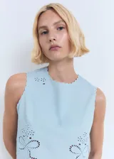 Top de algodón celeste sin mangas, con diseño crop, cuello redondo, tirantes anchos y terminaciones festoneadas. Presenta detalles bordados con motivos perforados en el frente y cierre de botón en el cuello.