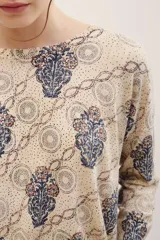 Sweater de punto color beige con estampado geométrico y floral en tonos azules y burdeos, de manga larga y cuello redondo.