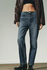 Jeans de mujer, tiro alto, color azul medio con efecto desgastado (lavado claro en muslos y oscuro en bordes). Corte recto y ancho (mom fit) con cinco bolsillos y cierre frontal de botón y cremallera.