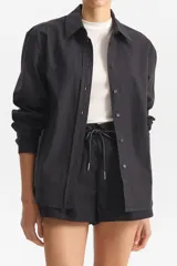 Camisa de manga larga con cuello, de corte recto y patrón a cuadros pequeños en tonos oscuros (negro y gris/marrón). Se lleva abierta sobre una camiseta blanca.