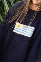 Sweater tejido a mano de color azul marino con diseño de la bandera de Uruguay en el centro del frente. Presenta un calce relajado, cuello redondo y terminaciones simples en puños y dobladillo.