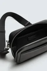 Bandolera negra con textura grabada, compartimento principal con cierre de cremallera, bolsillo interior con cremallera, bolsillo plano frontal, asa de hombro ajustable y extraíble.