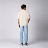 Remera oversize de lino entramado color blanco off-white, con cuello redondo, mangas cortas de hombro caído y etiqueta aplicada en el borde inferior.