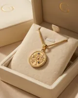 Collar de acero con baño de oro, compuesto por una cadena de eslabones finos y un dije circular con diseño de árbol de la vida grabado, decorado con pequeñas circonias de colores.