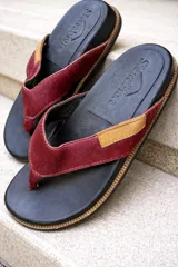 Chinelas de cuero con pelo en color bordó, con base de cuero negro y detalle de etiqueta en cuero tostado. Diseño de tiras anchas con textura.
