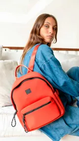 Mochila de neopreno color naranja con detalles en cierres negros. Cuenta con asa de mano, correas regulables, bolsillo frontal con cierre y bolsillo trasero de apertura vertical. El interior posee buena capacidad con dos bolsillos con cierre y uno abierto con división.