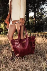 Cartera de cuero color bordó, tipo tote bag, con doble asa de hombro y hebillas decorativas a los costados. Incluye doble bolsillo y colgante interno para llaves.