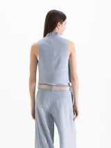 Chaleco Capri de corte cropped y calce al cuerpo, confeccionado en tejido color negro. Presenta escote redondo pronunciado con detalle de volados tableados que recorren el contorno y cierre cruzado delantero con seis botones metálicos. Incluye bolsillos frontales ojal.