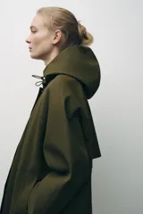 Cazadora impermeable de acabado engomado en color amarillo, con capucha ajustable, cierre frontal con botones a presión, bolsillos laterales y mangas largas ajustables.