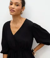 Blusa peplum de viscosa negra con escote en V cruzado, mangas cortas abullonadas con elástico en los puños y cordón ajustable en la cintura.