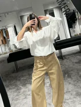 Camisa blanca de textura rayada con cuello mao y cierre frontal de botones. Presenta mangas largas abullonadas con puños anchos y corte holgado.