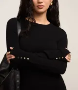 Suéter negro ajustado de punto con cuello redondo, mangas largas y botones dorados en los puños.