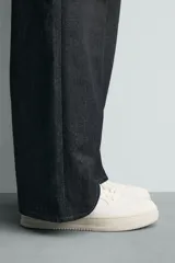 Zapatilla deportiva de estilo retro con diseño de paneles en combinación de colores crema, verde azulado y detalle en rojo en el talón. Presenta suela con volumen y cierre con cordones.