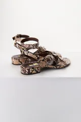 Sandalias de cuero color marrón chocolate, con tira ancha sobre el empeine con detalle de hebilla trenzada plateada, pulsera al tobillo con hebilla metálica y taco bajo cuadrado.