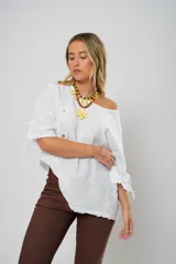 Blusa blanca de lino con corte asimétrico, mangas 3/4 con botones y cuello redondo amplio.