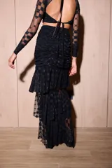 Falda larga de encaje color negro, de silueta ajustada con volados escalonados y abertura lateral pronunciada.