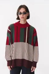 Buzo oversize de tejido de punto con diseño de bloques y rayas verticales en colores rojo, verde, bordó y crema. Presenta cuello alto tejido y terminaciones en rib en puños y ruedo.