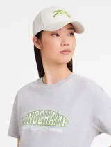 Gorra de béisbol color crema, con visera curva y logo bordado en verde claro.