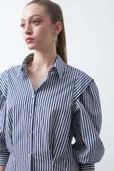 Camisa a rayas azules y blancas de manga larga, con cuello clásico y puños abotonados. Presenta un diseño entallado en la cintura.